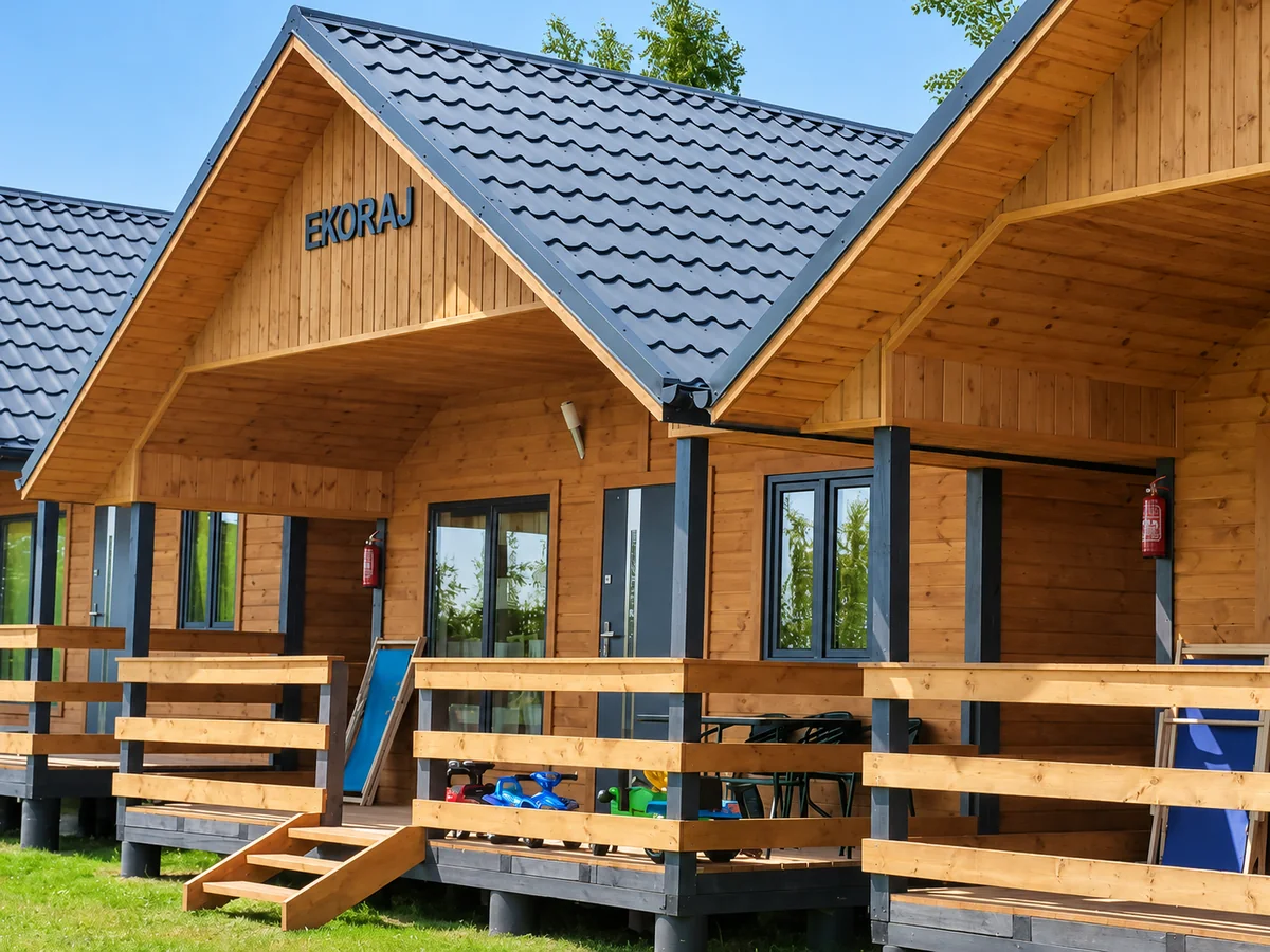 Fasada domku z napisem EKORAJ, ganek z drewnianą balustradą i ciemnym dachem